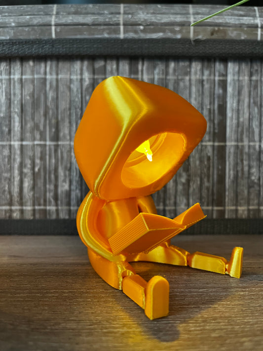 Lesender Gefährte Sunny aus gelbem PLA Silk+, 3D-gedruckte Dekofigur mit Licht, sitzt lesend auf einem Regal, stimmungsvolle Beleuchtung, Geschenkidee für Buchliebhaber, Club der lesenden Gefährten.
