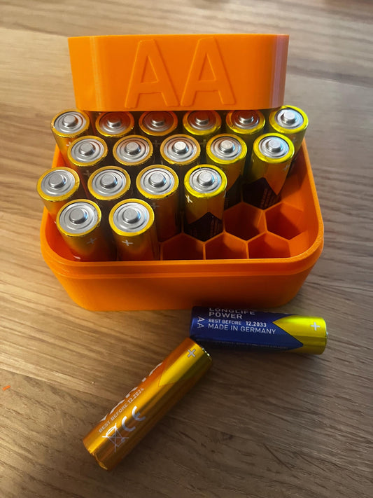Geöffnete Batteriebox mit 22 AA-Batterien, orange, auf Holztisch.